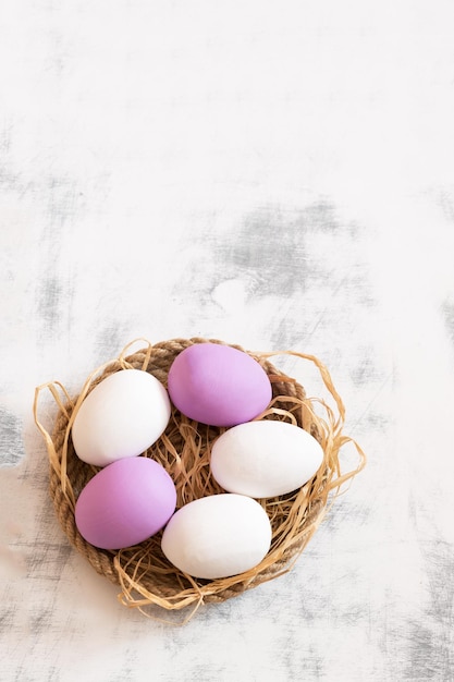 Белые и фиолетовые пасхальные яйца лежат на подносе из шпагата под ними сено