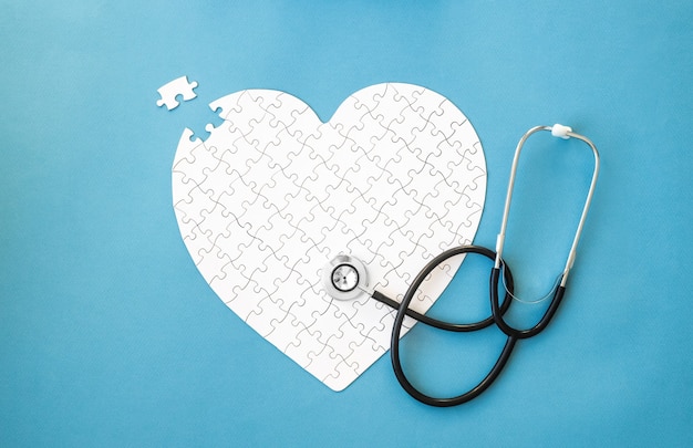 White puzzle in heart shape and stethoscope on blue background heart health concept