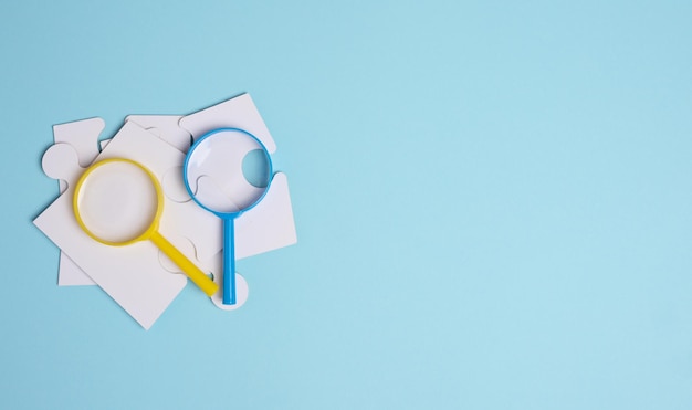 White puzzles and plastic magnifying glass on a blue background top view