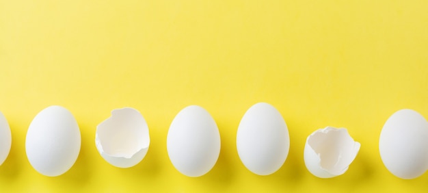 White raw chicken eggs lying in horizontal row with broken egg . Top view.