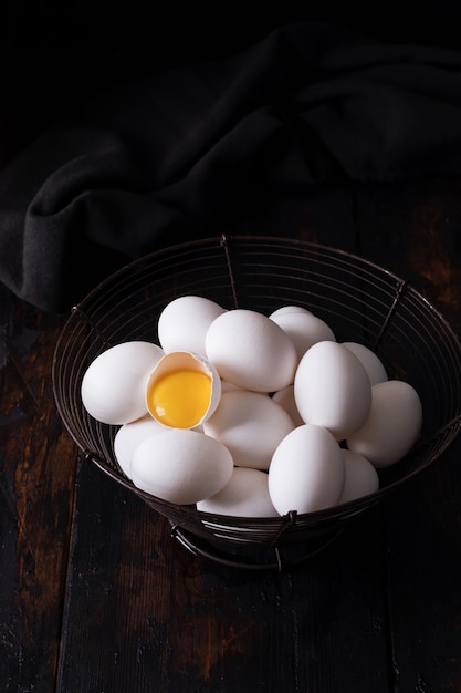 White raw chicken eggs in an old vintage basket on dark surface