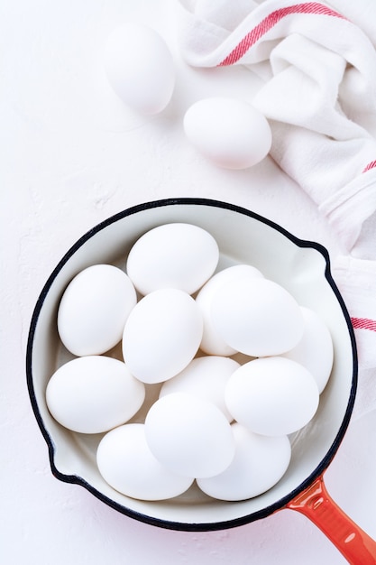 White raw chicken eggs in red pan . Top view.