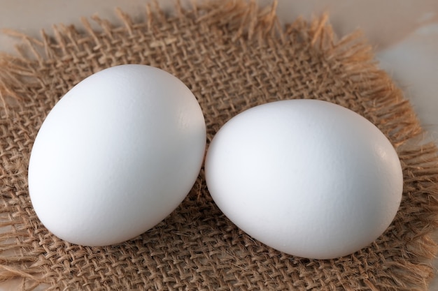 White raw eggs lie on the table on a burlap napkin close-up