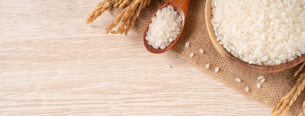 White raw rice in a bowl with the ear on the wooden table background.