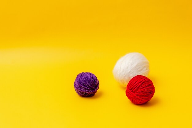 Photo white, red and blue balls of wool lie on a yellow background