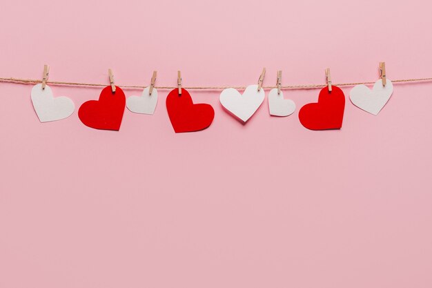 White and red heart pin on a rope on isolated pink background, love and valentine concept