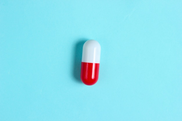 White red pill capsule on a blue background. Minimalism, medical concept, top view