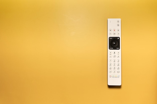 Foto un telecomando bianco con un pulsante nero su sfondo giallo.