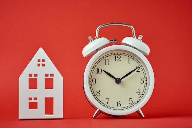 Photo white retro alarm clock and miniature house on red