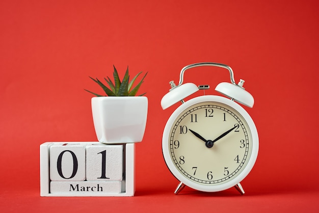 White retro alarm clock on red background and wooden calendar blocks