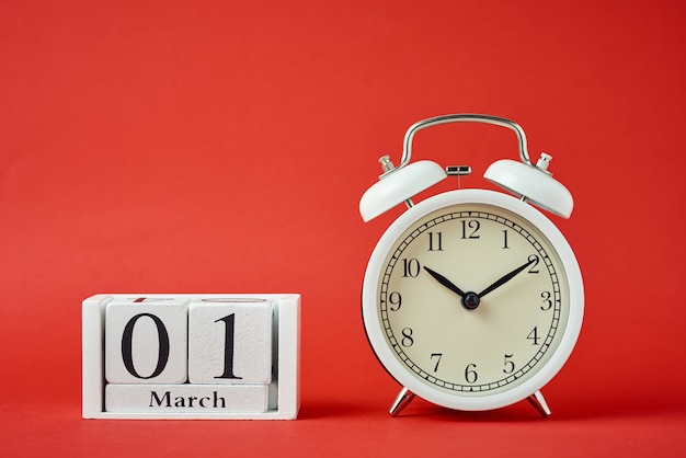 White retro alarm clock with bells and wooden calendar blocks with date 1 march on red