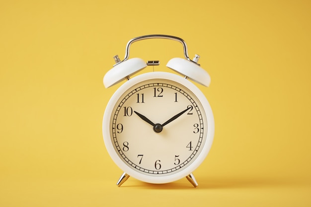 White retro alarm clock on the yellow with copy space. Time concept