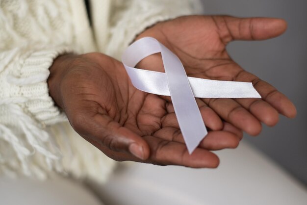 Photo white ribbon close-up in dark brown african hand skin for breast cancer concept on grey background