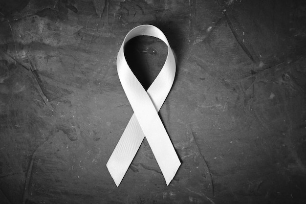 White ribbon on dark concrete background is symbol of protection of traditional family, problem of protecting women from violence.