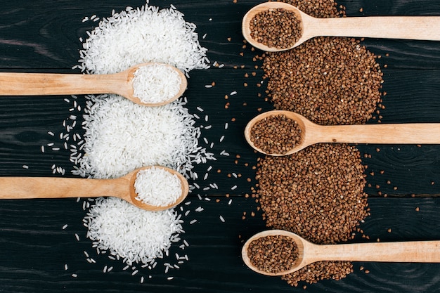 White rice and buckwheat groats in the wooden spoon on the black table