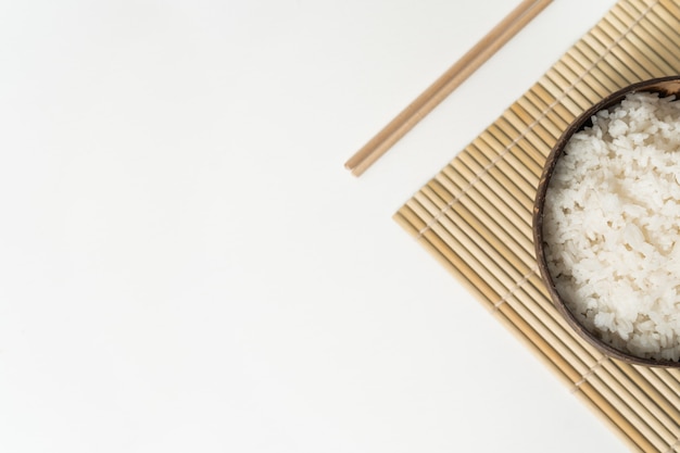 Photo white rice in a coconut bowl on a white background. minimalistic photo with rice and bamboo chopsticks.