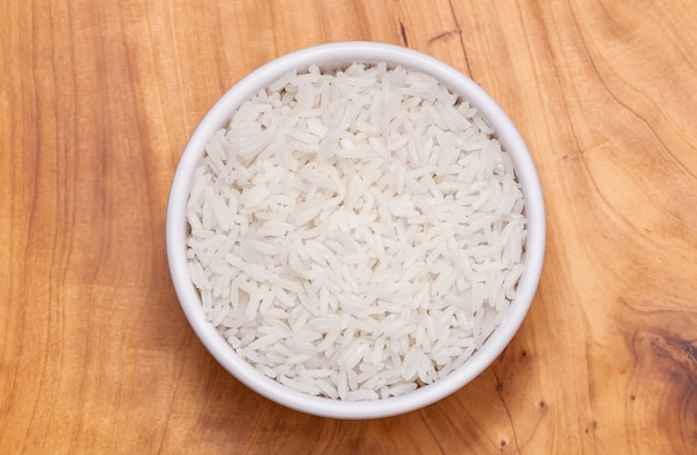 white rice cooked in a white bowl on a wooden cutting board top view photo