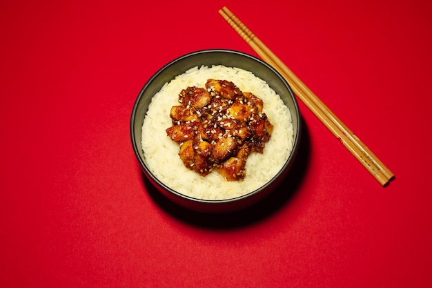 White rice with chicken and chopsticks on the red background