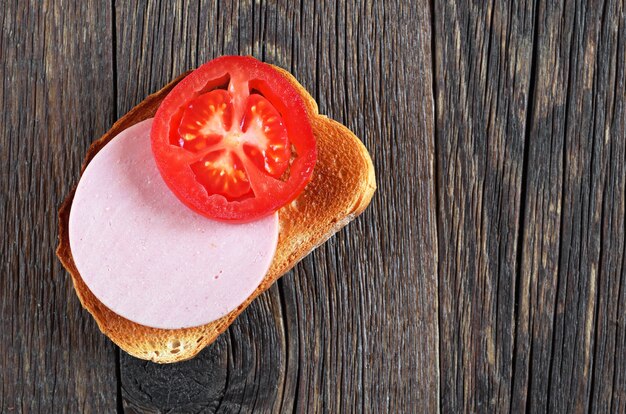 White roasted bread with boiled sausage and tomato on wooden table