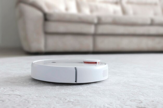 White robot vacuum cleaner on carpet. Modern smart device cleaning floor.