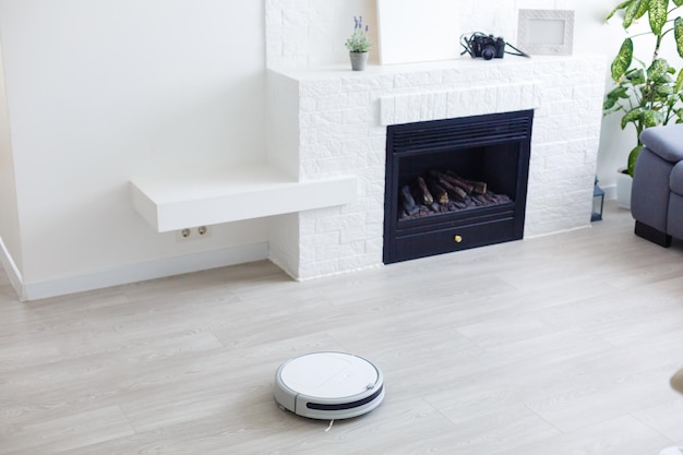 white robot vacuum cleaner cleans the floor from debris,home cleaning with an electric vacuum cleaner,vacuum cleaner electric robot cleaning technology,top view of a robot vacuum cleaner