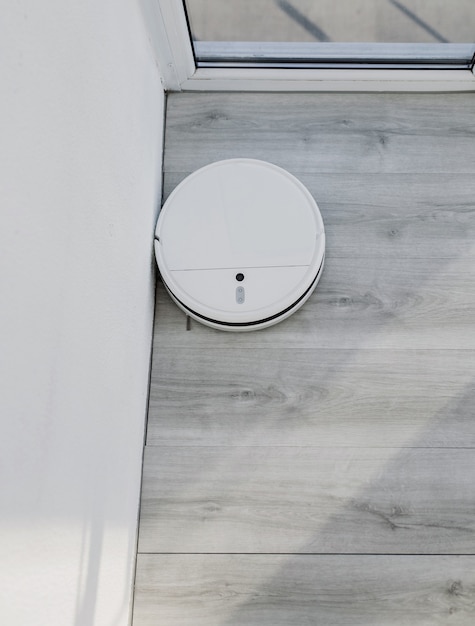 White robot vacuum cleaner cleans the floor. Home cleaning with an electric vacuum cleaner. Top view of a robot vacuum cleaner