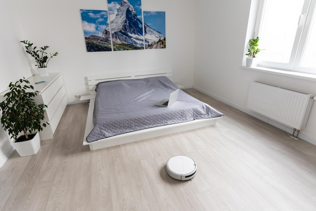 White robot vacuum cleaner device cleaning floor from crumbs at home.