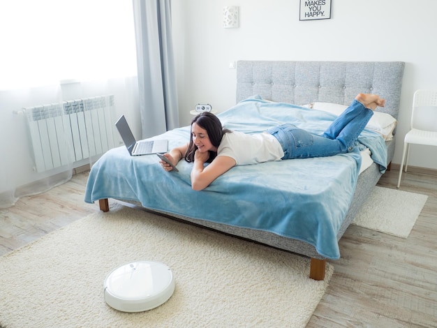 White robotic vacuum cleaner cleaning the floor while woman using laptop