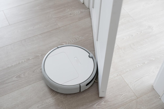 Aspirapolvere robotico bianco sul pavimento in laminato che pulisce la polvere all'interno del soggiorno. tecnologia di pulizia elettronica intelligente.