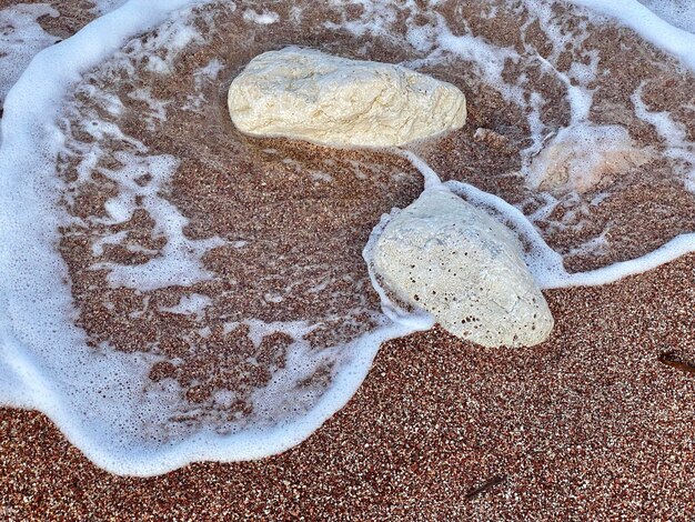 A white rock is on a beach with the water foaming around it.