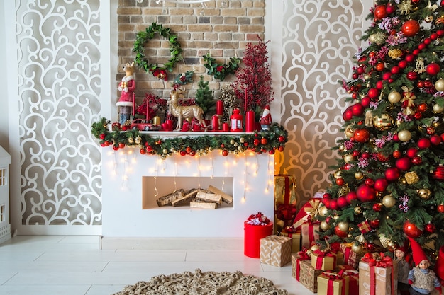 White room interior in red tones with New Year tree decorated, present boxes and artificial fireplace