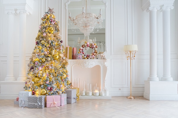 White room interior with New Year tree decorated, present boxes and artificial fireplace