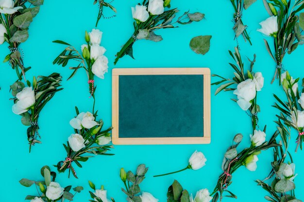 White roses and blackboard on green background. Above view