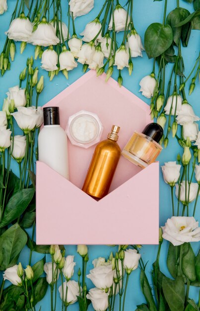 White roses and perfume bottle with pink envelope on blue surface. Above view