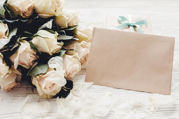 Foto rose bianche con carta vuota e confezione regalo su fondo in legno spazio per il testo mockup di biglietto di auguri floreale invito a nozzefelice festa della mamma concetto san valentino