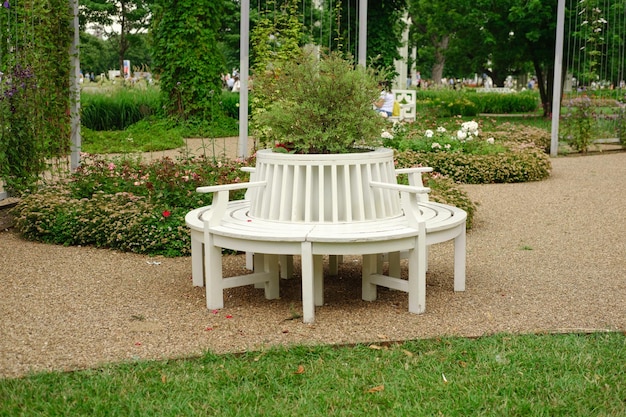 Белая круглая скамейка для отдыха в цветущем парке в черте города. Магазин для отдыха в городах.