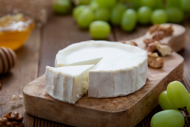 White, round cheeses on wooden with honey and grapes.