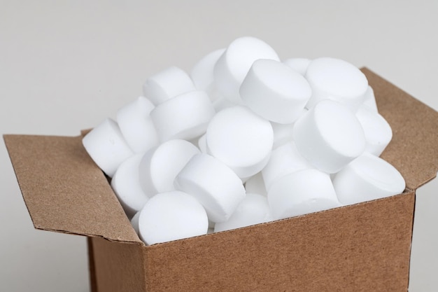 White round dishwasher salt tablets in a box A set of white capsules in an open box top view