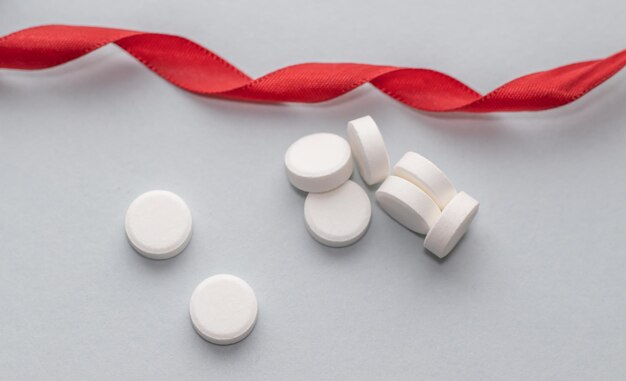 white round pills on grey background and a red lace near health care concept medicine