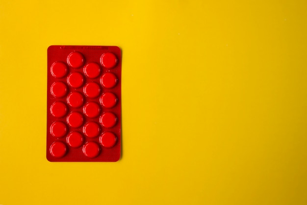 White round pills in red packaging on yellow