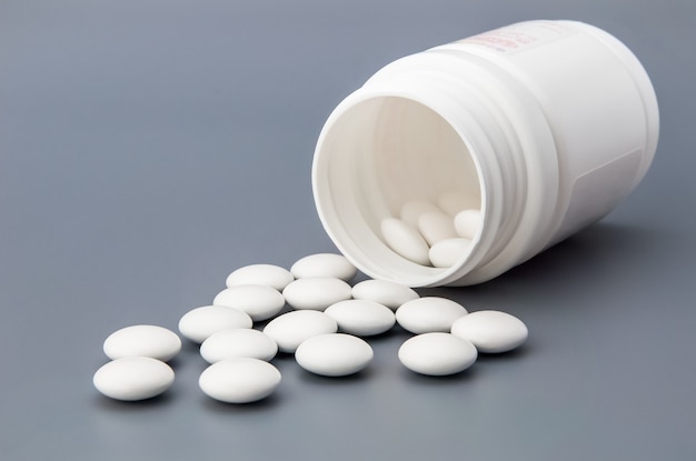 White round pills scattered from a white jar.