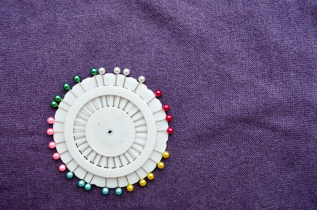Photo white round pin needle bed with colored needles on a background of purple cloth