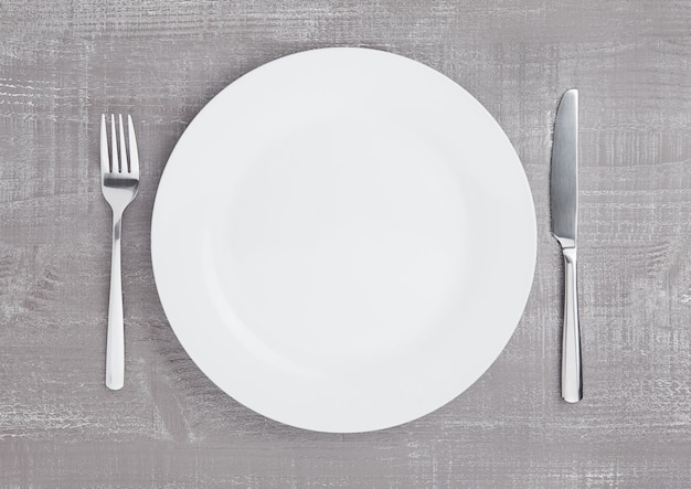 White round plate with fork and knife on wooden board surface