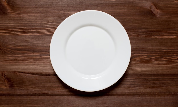 Белая круглая тарелка на деревянном фоне.