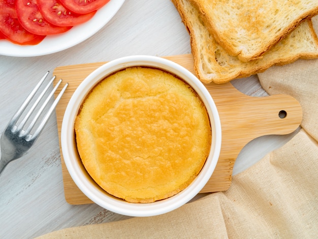 White round ramekin with oven-baked omelet of eggs and milk, with a crust, on white wooden table