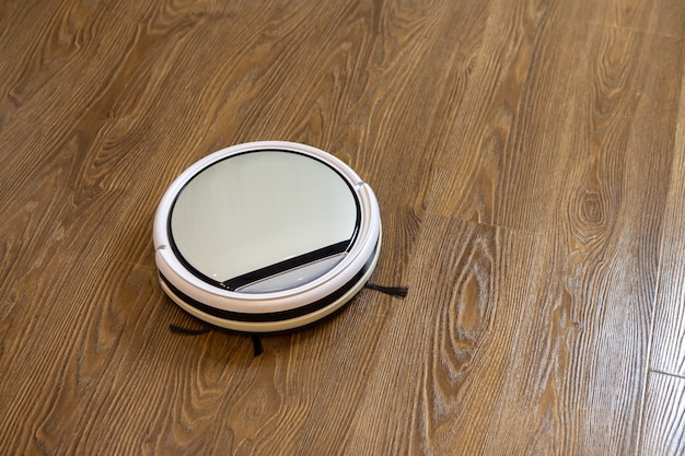 White round wireless robot vacuum cleaner on brown laminate floor