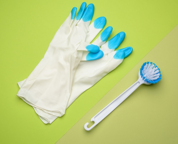 White rubber gloves for cleaning, brushes on a green background, flat lay