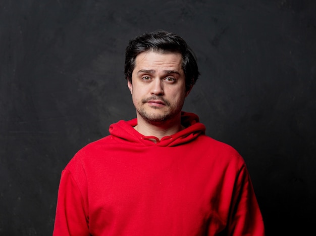 White sad guy in red sweatshirt on dark wall