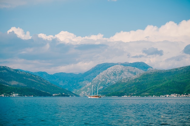 White sailing yacht sails along the kotor bay against green mountains on a bright