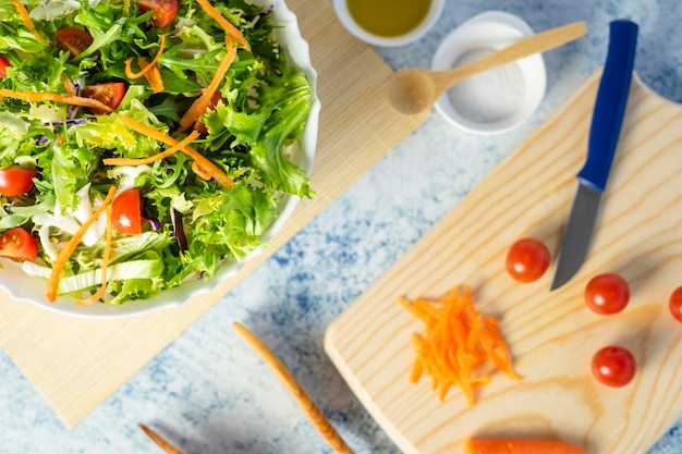 White salad bowl full of vegetables together with some ingredients. Oil, salt, tomatoes.